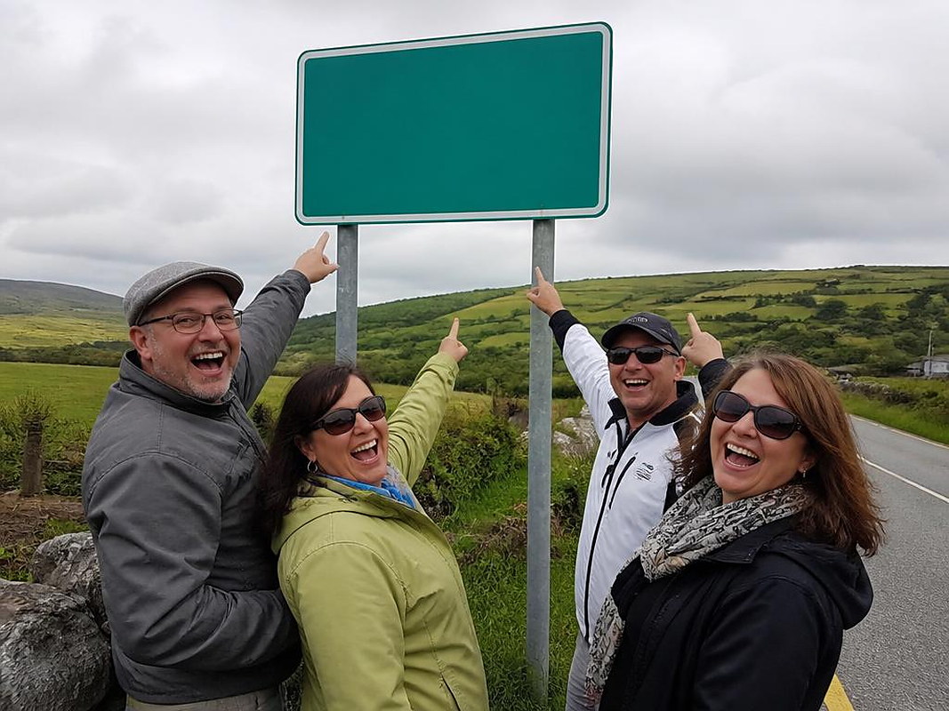 Tourists laughing and pointing up at a green Irish road sign